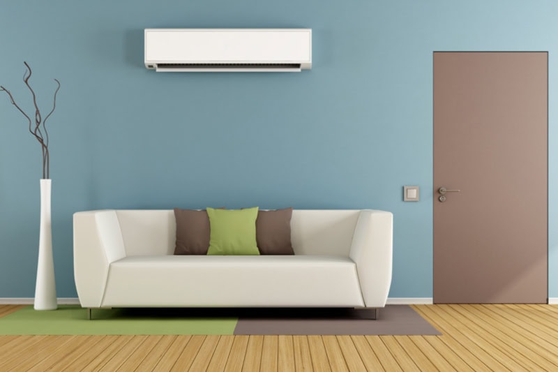Is It Worth Installing a Ductless Air Conditioner? Photo of a white couch in front of a blue wall and air conditioner mounted above.